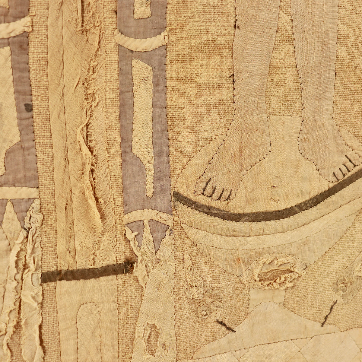 A close-up of a textured, distressed textile featuring beige and tan woven fabric with stitched details, frayed edges, and muted taupe accents.