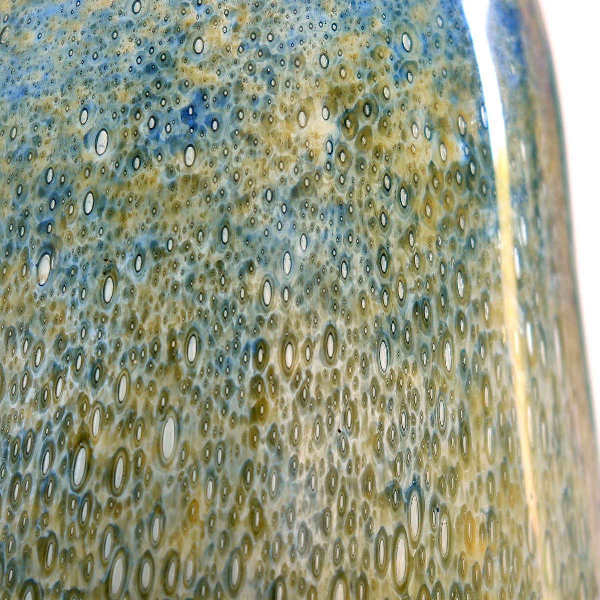 Close-up of a glossy ceramic vase featuring a dense pattern of small circular bubble-like dots in blue, gold, and cream tones.