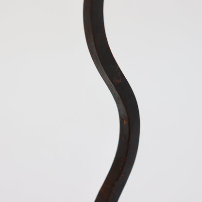 Detail of the curved hand-forged iron stem showing its flattened faces and dark patina.