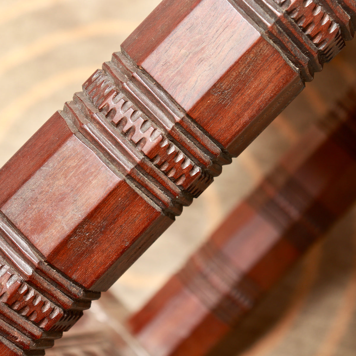 Close-up of a faceted hardwood support with carved decorative bands and a reddish-brown finish.