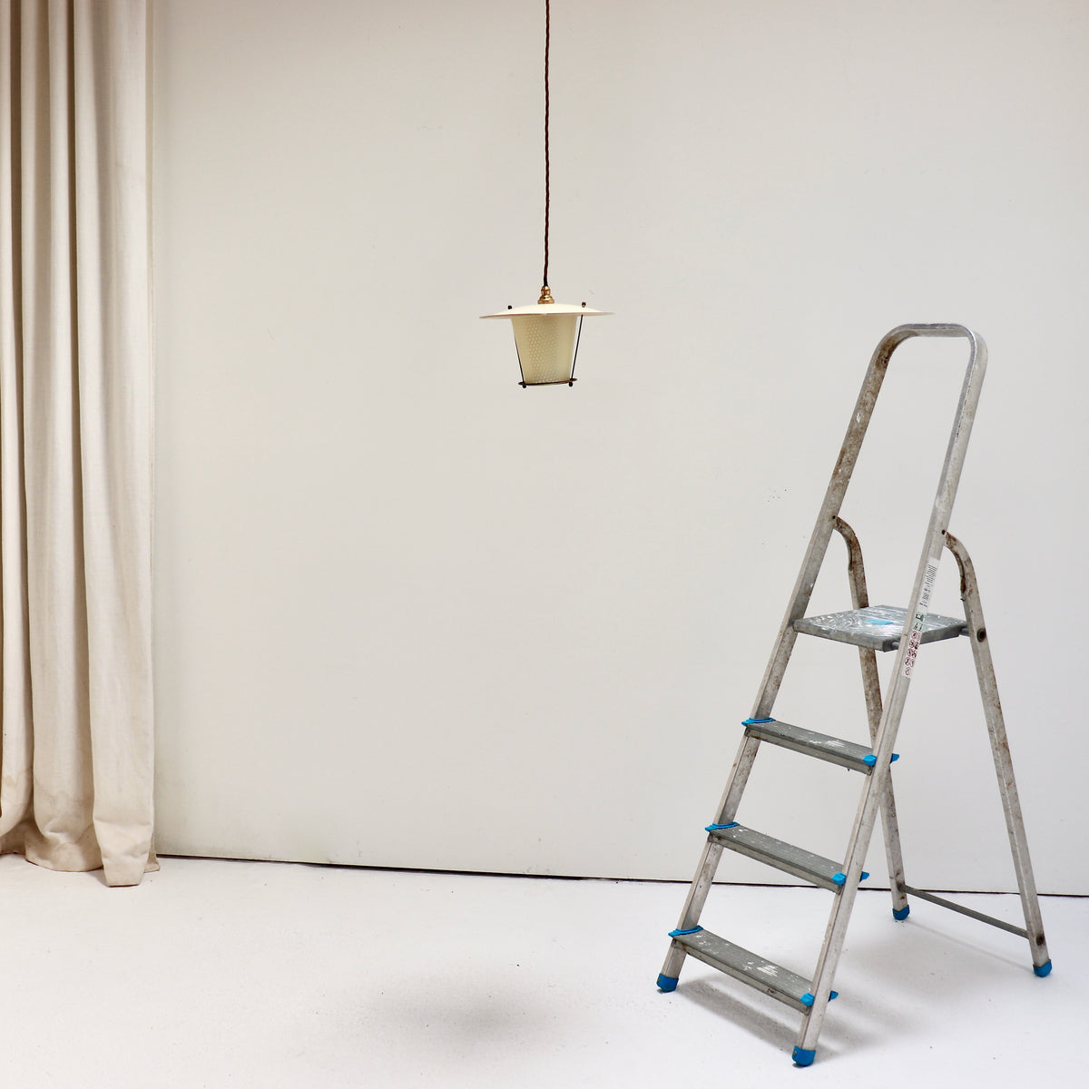 Small French pendant suspended beside a stepladder, showing its scale and long brown braided cable.
