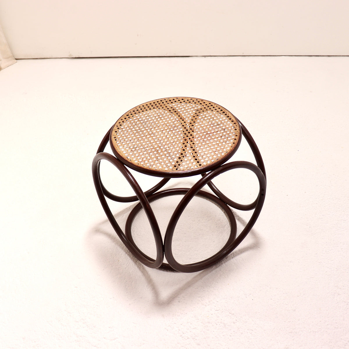 A small round side stool with a natural woven cane seat and a dark brown curved metal frame, photographed on a white surface against a white background.