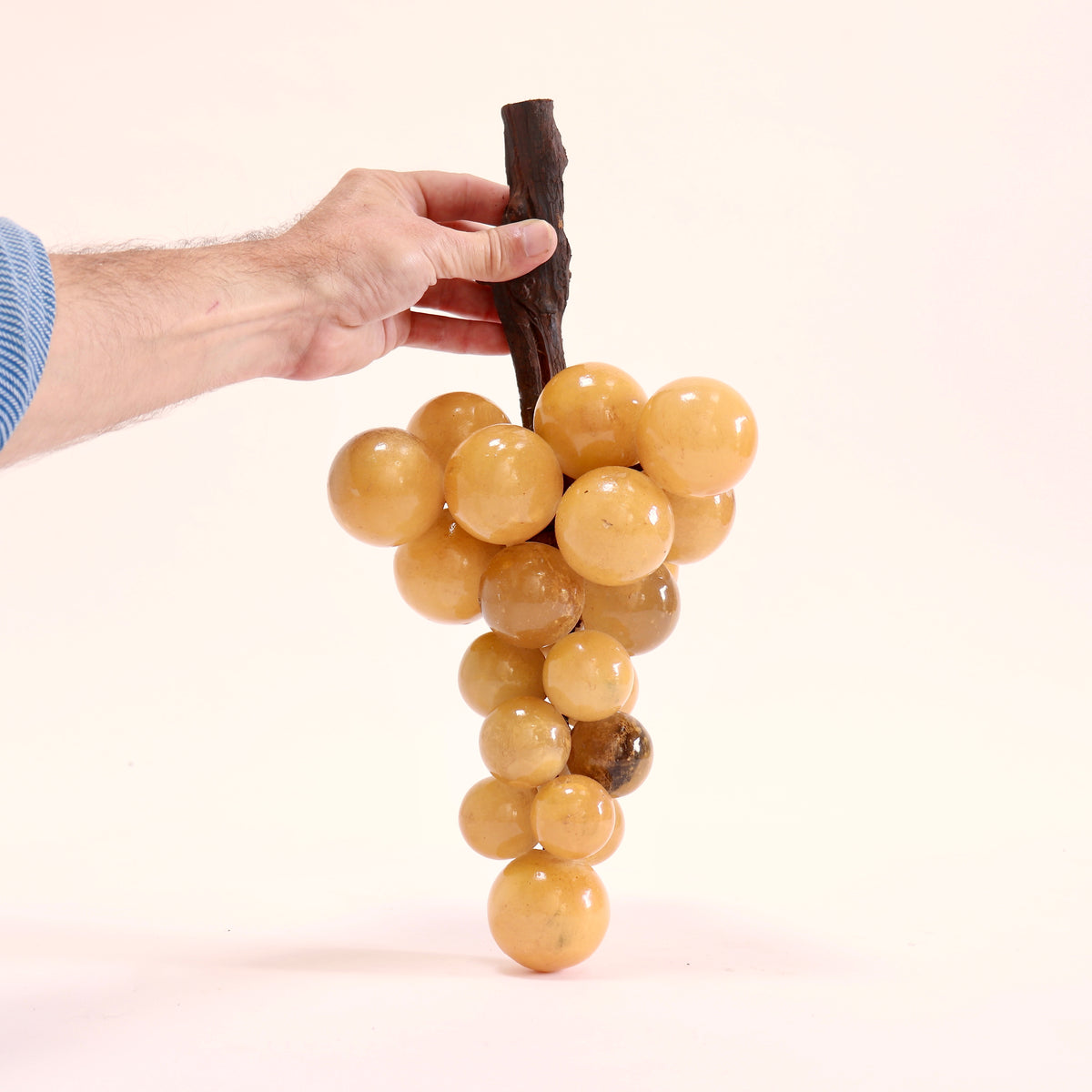 Large bunch of honey-toned alabaster grapes held upright by its dark wooden stem to show scale.