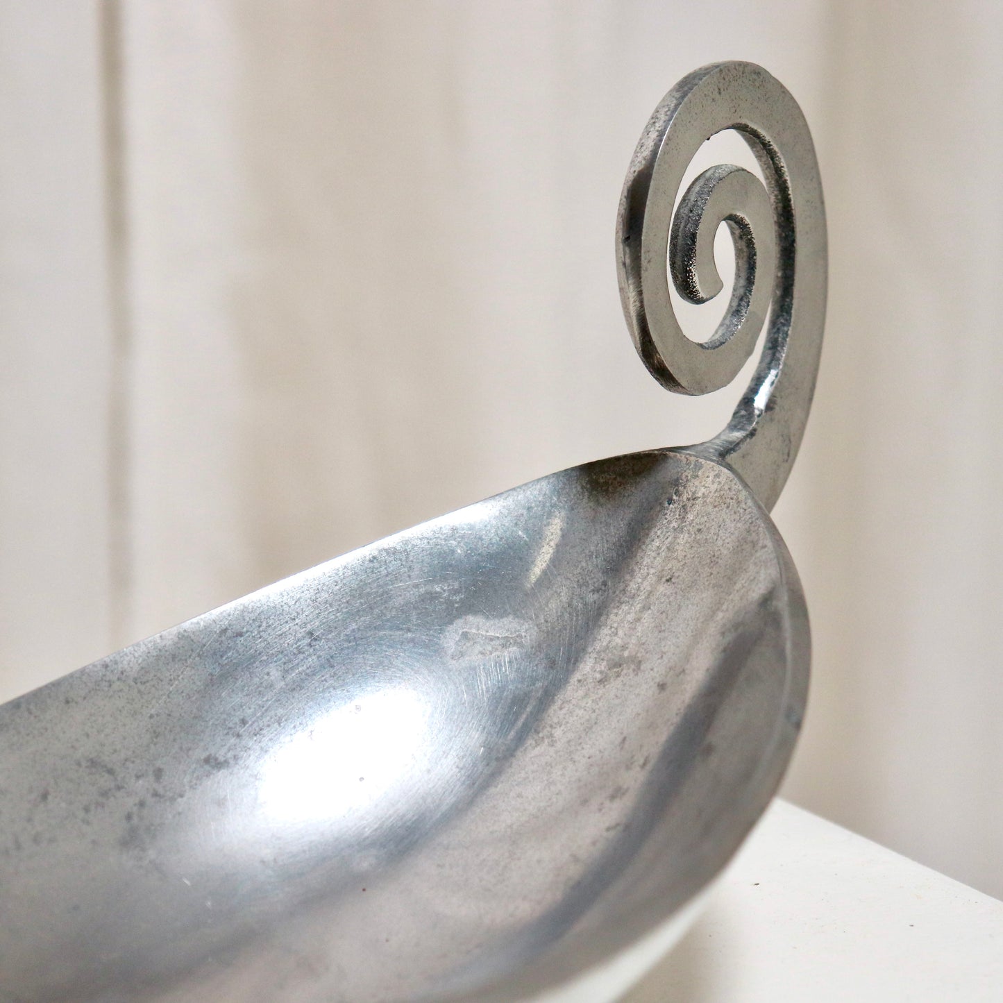 End-on view highlighting shallow bowl and handle curl.
