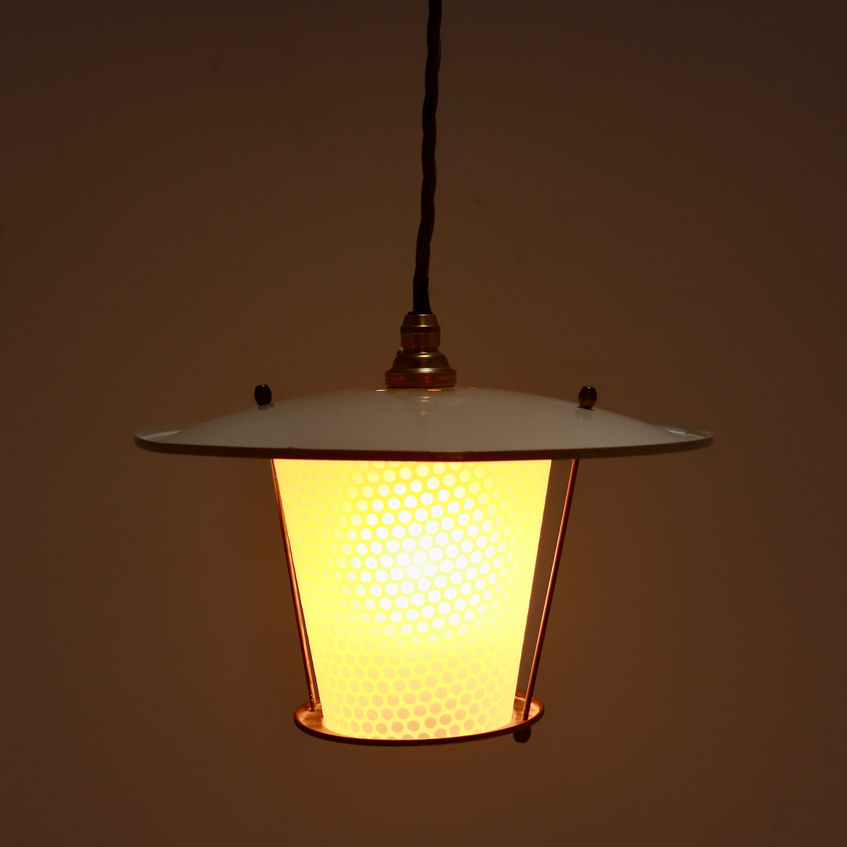 Illuminated French pendant showing the dotted glass glowing beneath its cream enamel shade.