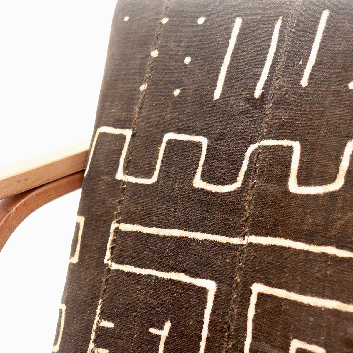 Close-up of antique Malian mud cloth across a Heal’s armchair seat, showing cream geometric patterns and stitched joins beside the wooden frame.