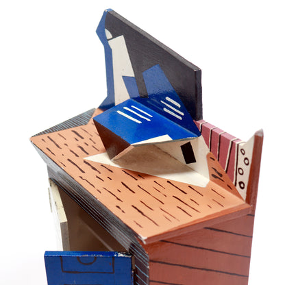 A handcrafted wooden pop-up model of a house and treehouse structure, featuring a blue roof, brown wood-grain textured sides, and cream-colored details, set against a plain white background.