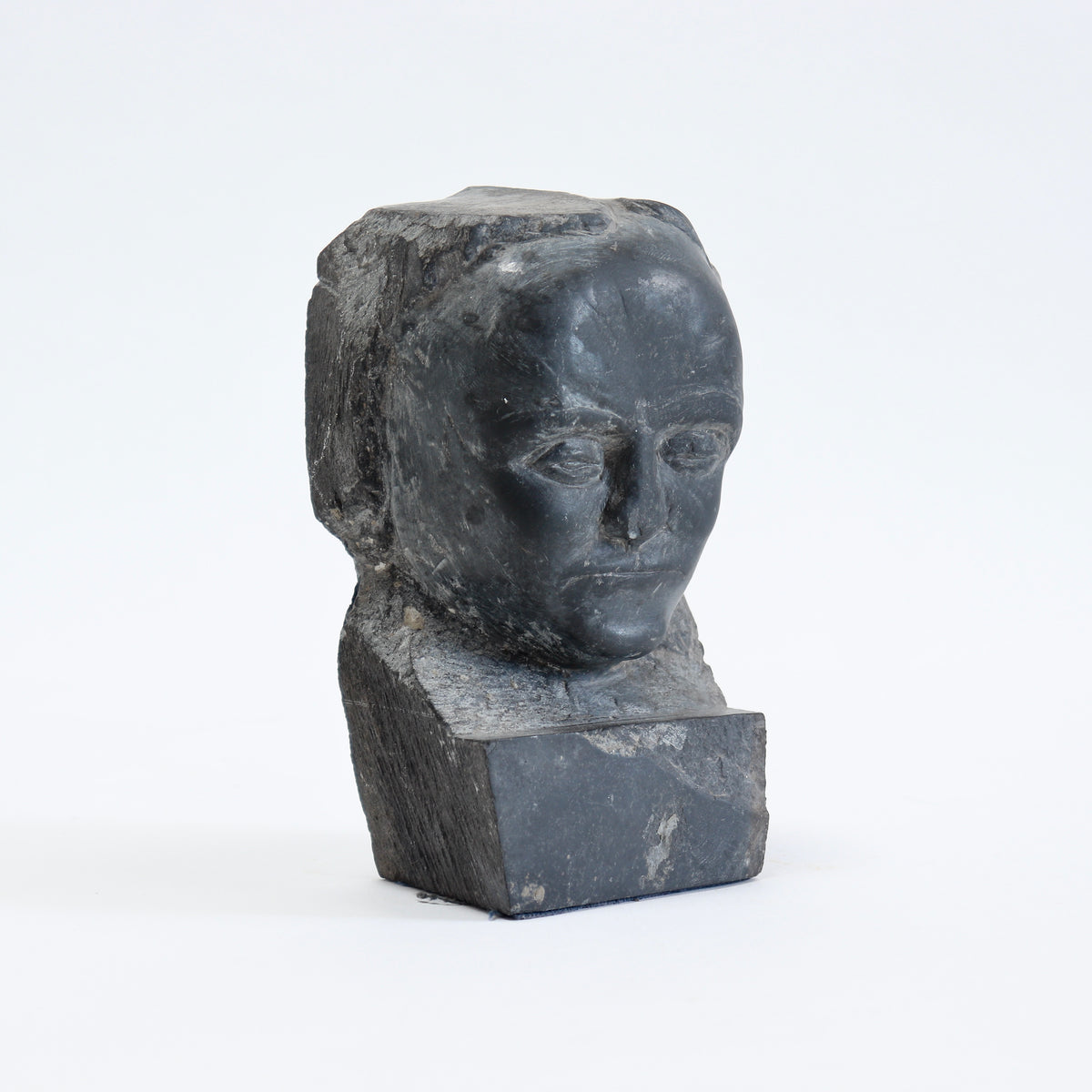Three-quarter view of the carved slate face emerging from a rough rectangular block.