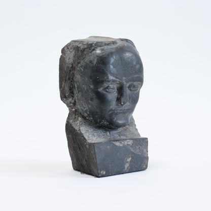 Three-quarter view of the carved slate face emerging from a rough rectangular block.