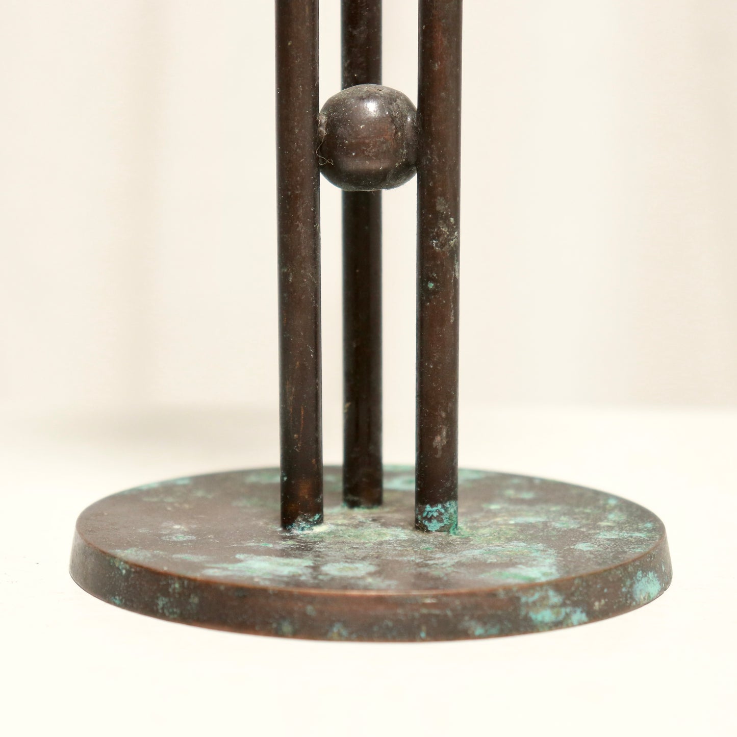 Bronze sculpture with three vertical bars and a round base on a light background