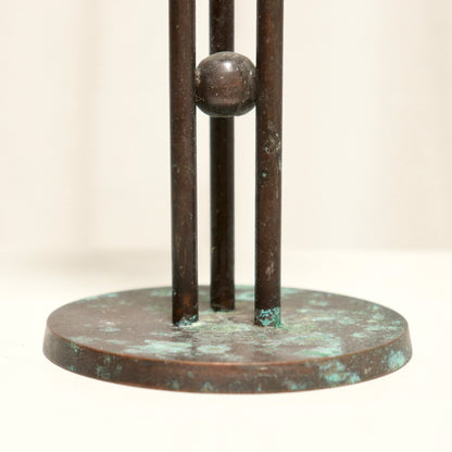 Bronze sculpture with three vertical bars and a round base on a light background
