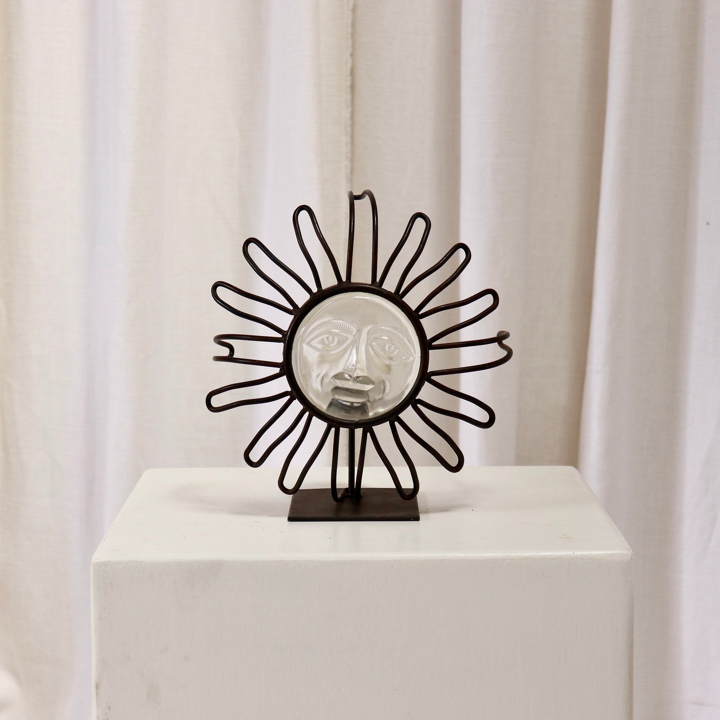 Wrought-iron sunburst candle holder with pressed-glass face on a plinth.