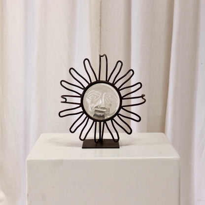 Wrought-iron sunburst candle holder with pressed-glass face on a plinth.