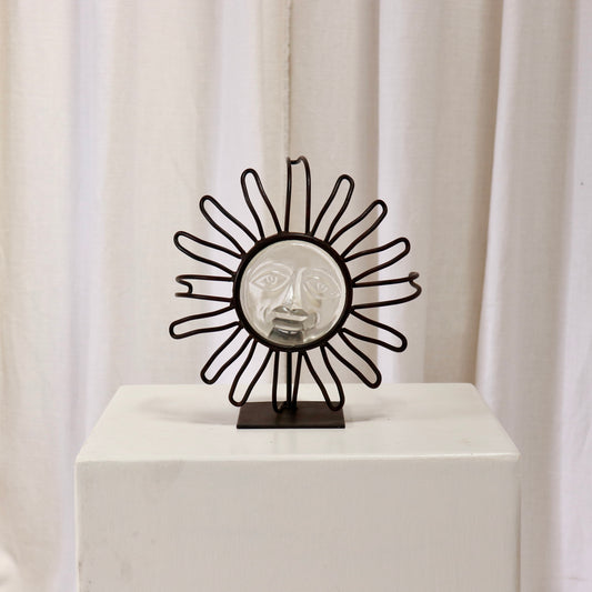 Wrought-iron sunburst candle holder with pressed-glass face on a plinth.