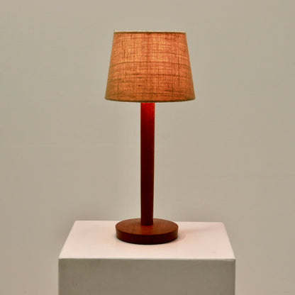 “Vintage teak lamp lit with hessian shade, warm glow”