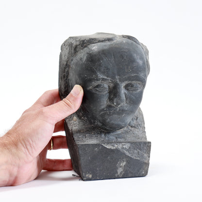 Small carved slate portrait bust beside a hand to show its scale and rough stone surround.