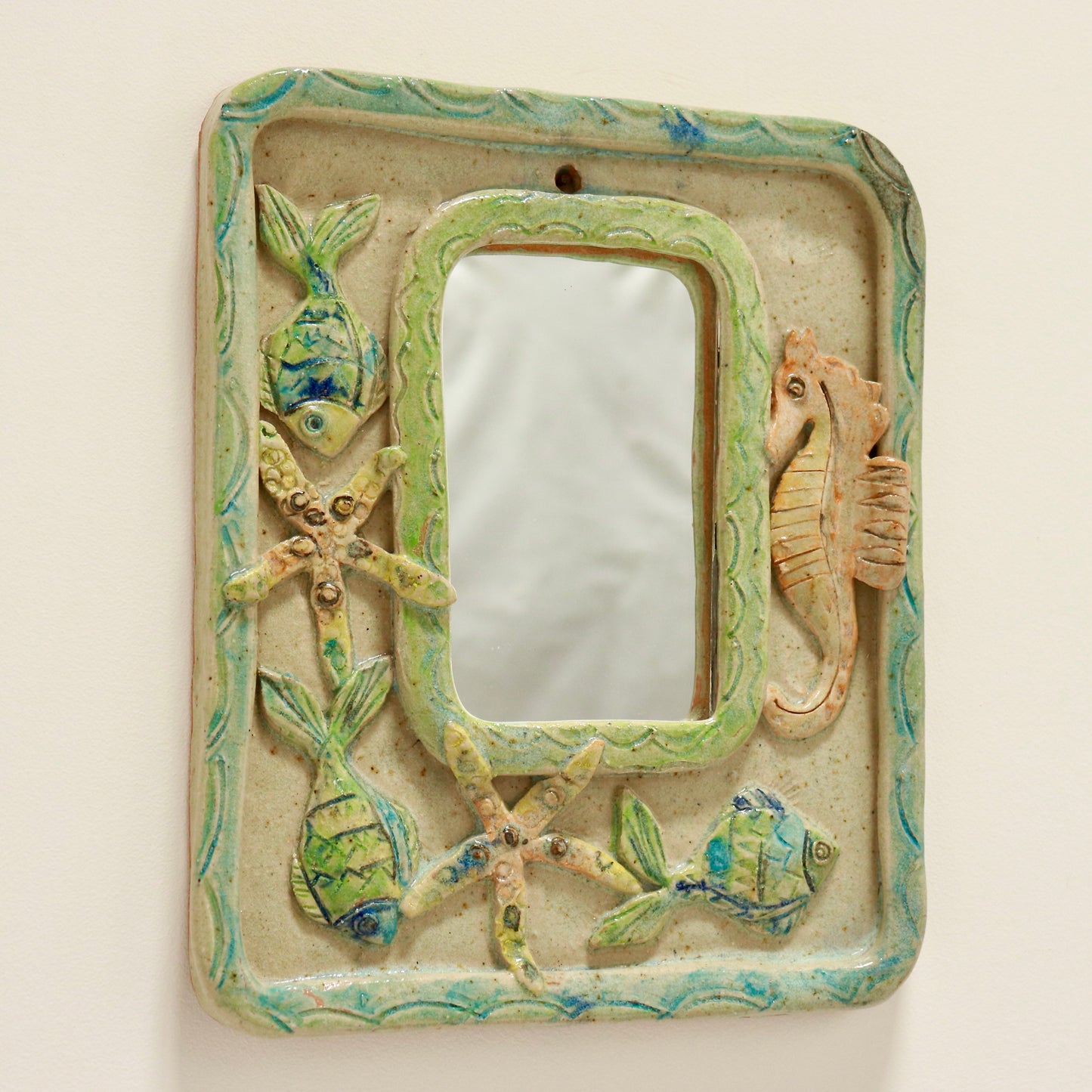 “Angled view of signed folk art ceramic mirror showing underwater motifs”