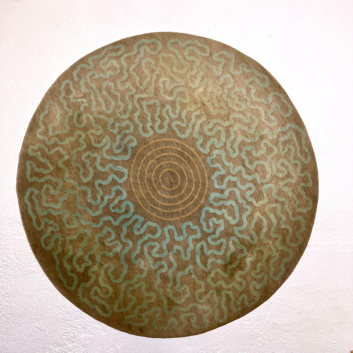 Overhead view of the complete circular rug showing its abstract aqua pattern, central rings and areas of fading.