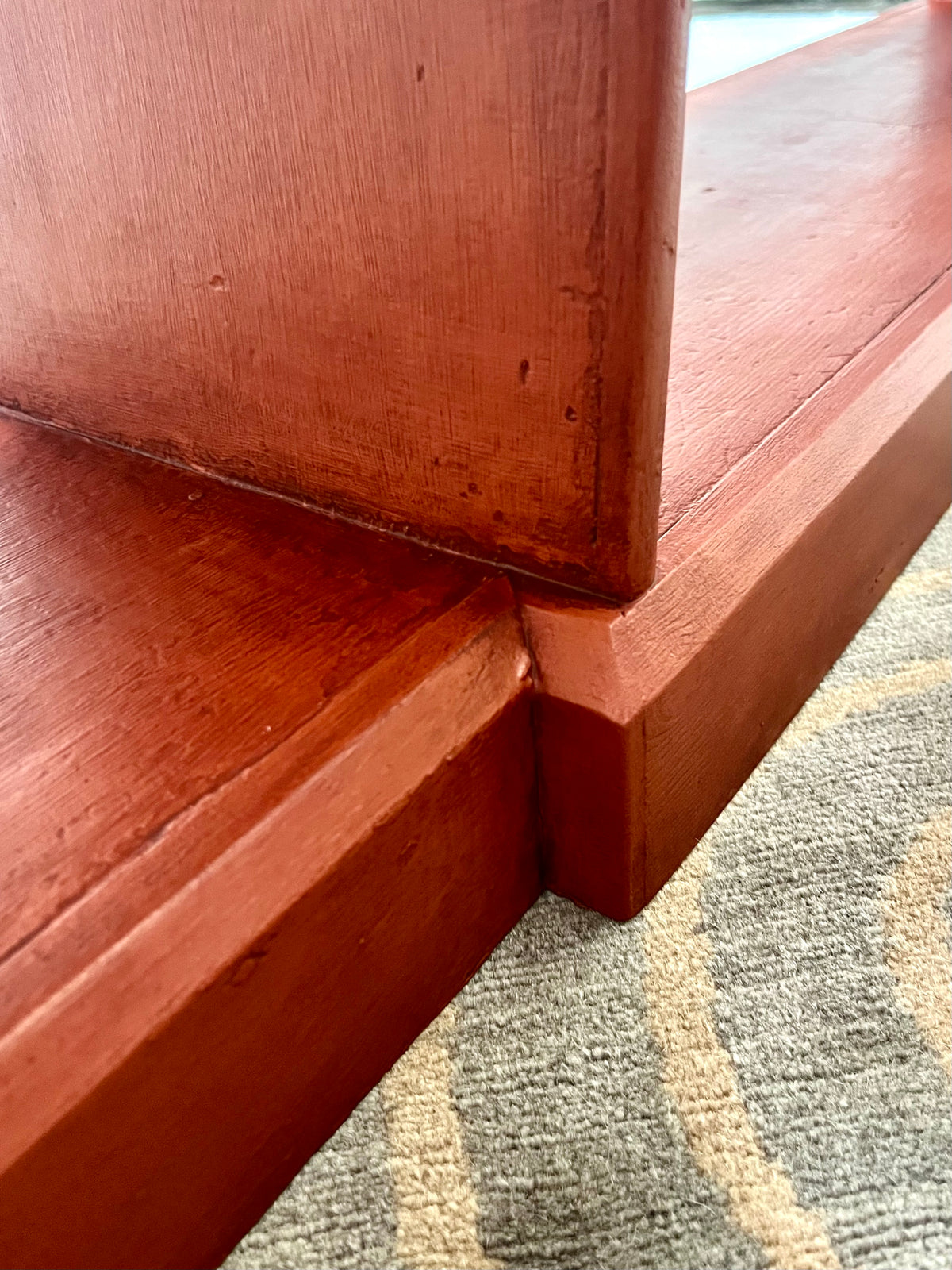 Close-up of a reddish-brown wooden furniture corner meeting a patterned gray and beige carpet.